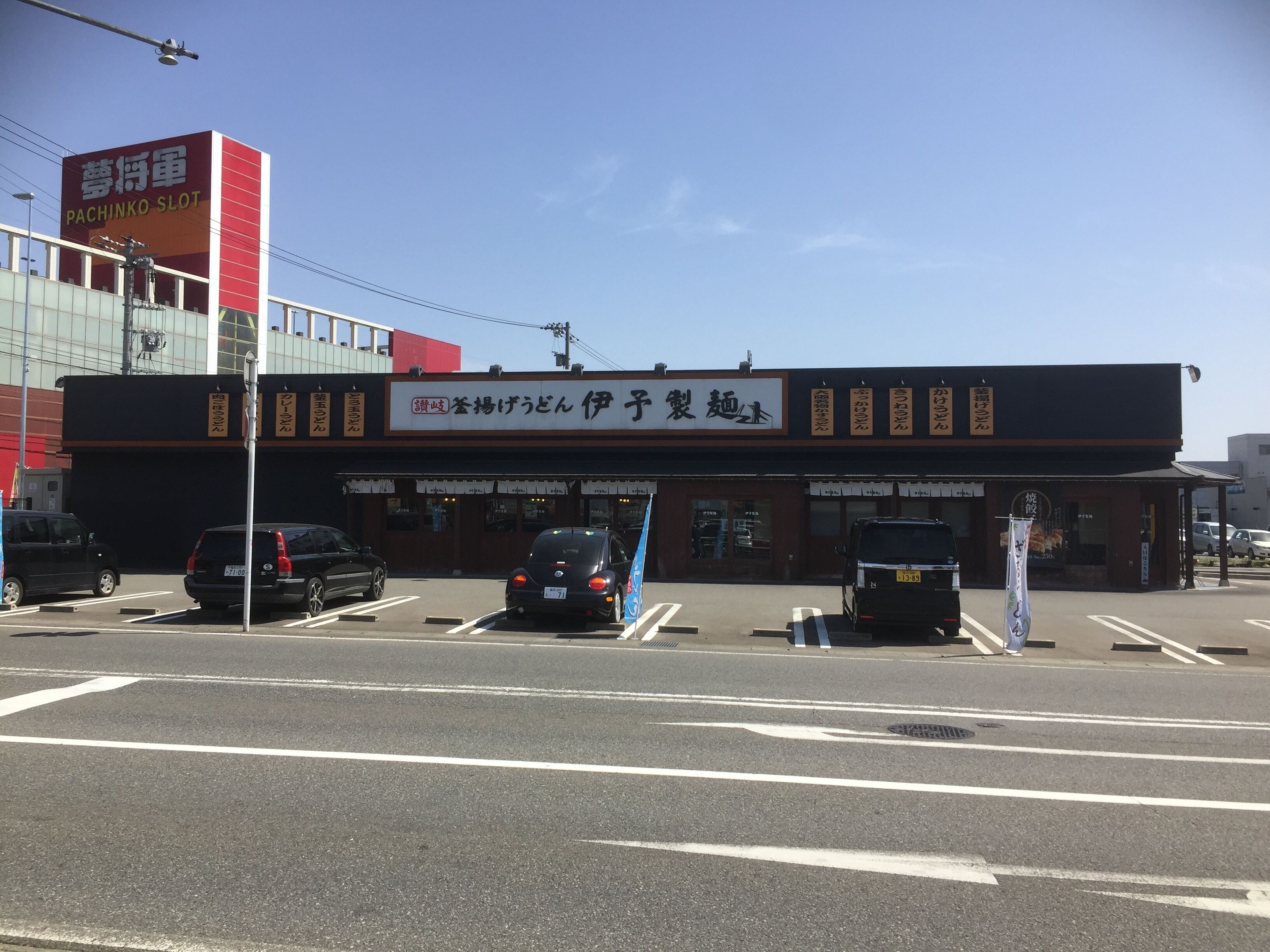 Un edificio con señalización en idioma extranjero, un estacionamiento con coches y un cielo despejado.