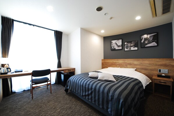 A hotel room with a bed, a desk, a chair, and a window with curtains.