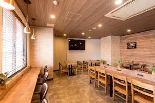 Un restaurante con mesas y sillas de madera, pared de ladrillo e iluminación empotrada en el techo.