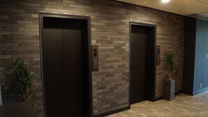 Two elevator doors with a modern brick wall design and a potted plant beside each. - Hotel Cooju Fukui (Sakai)
