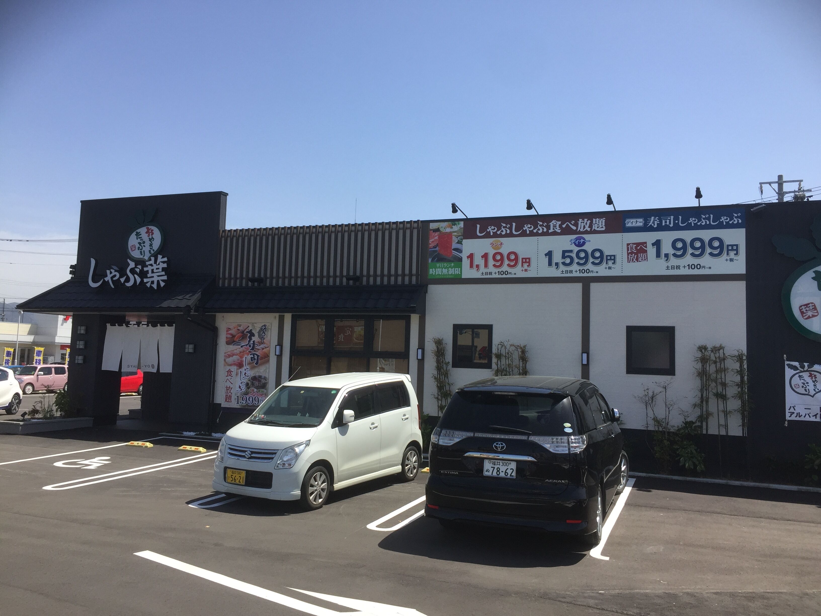 A parking lot with two cars parked in front of a building with Japanese signage.