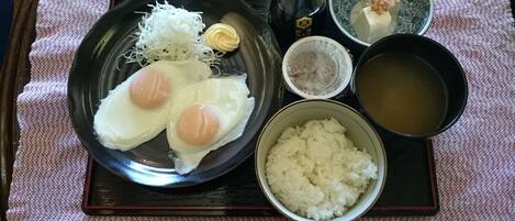 Uma refeição japonesa tradicional com arroz, dois ovos, legumes ralados e uma pequena tigela de sopa em uma bandeja.