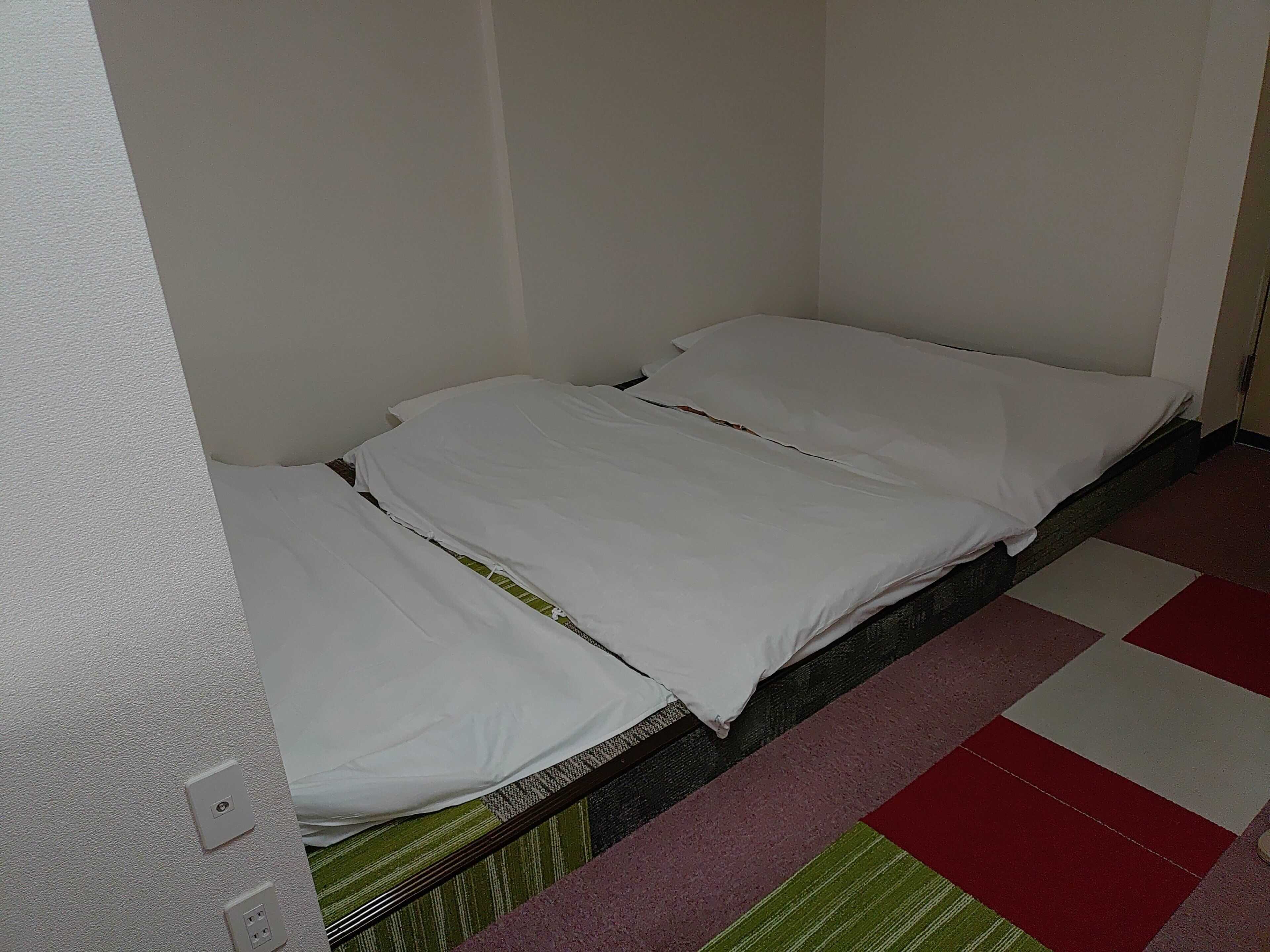 Ein Einzelbett mit weißer Bettwäsche in einem Zimmer mit Schachbrettmuster-Boden.