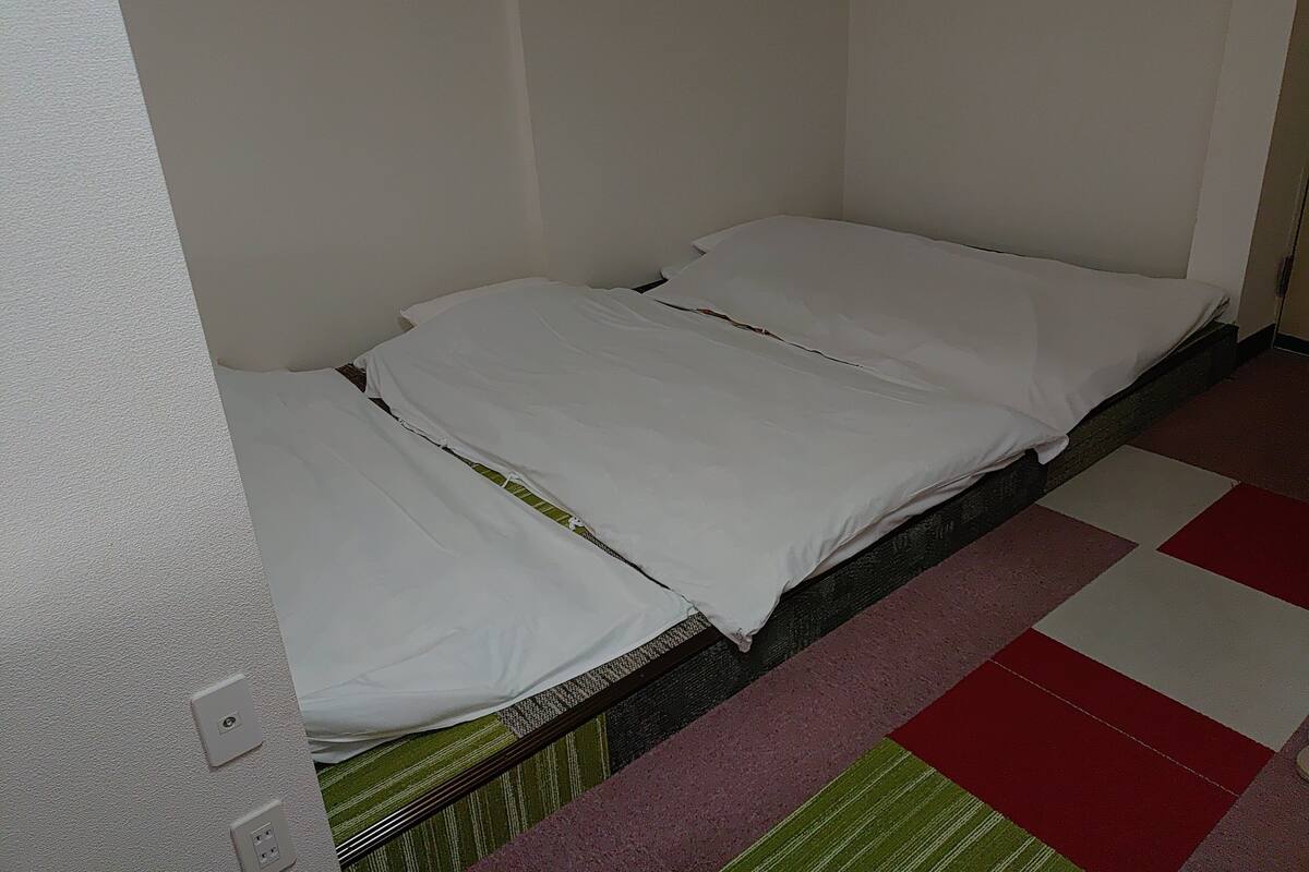 Una cama individual con ropa de cama blanca en una habitación con suelo a cuadros.