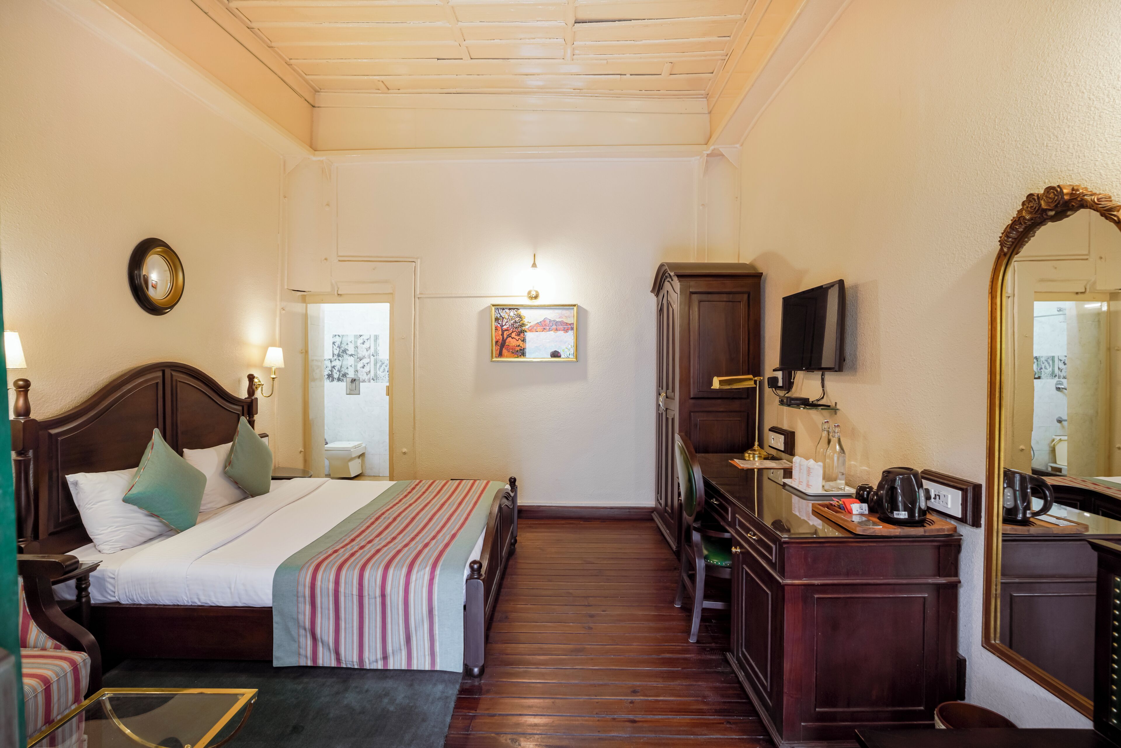 A hotel room with a bed, a desk, a television, a mirror, and a picture on the wall.
