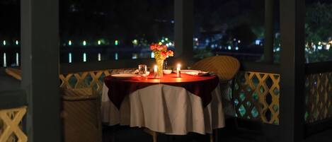 Une table dressée pour deux personnes, avec des bougies, un vase de fleurs et une vue sur le paysage urbain illuminé la nuit.