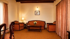 A living room with a sofa, armchairs, a coffee table, and a lamp. - The Grand Hotel Nainital (Nainital)
