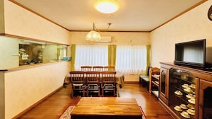 Una sala de estar con una mesa de comedor, sillas, un televisor y un mueble con vajilla.