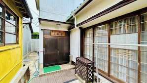 Una casa tradicional japonesa con una puerta de madera, un felpudo verde en la entrada y una pequeña mesa de madera.