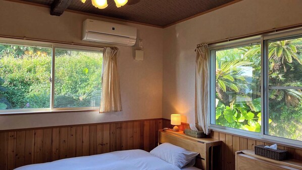 Un dormitorio con cabecera de madera, cama con ropa de cama blanca, unidad de aire acondicionado, lámpara de noche y una ventana con cortinas.