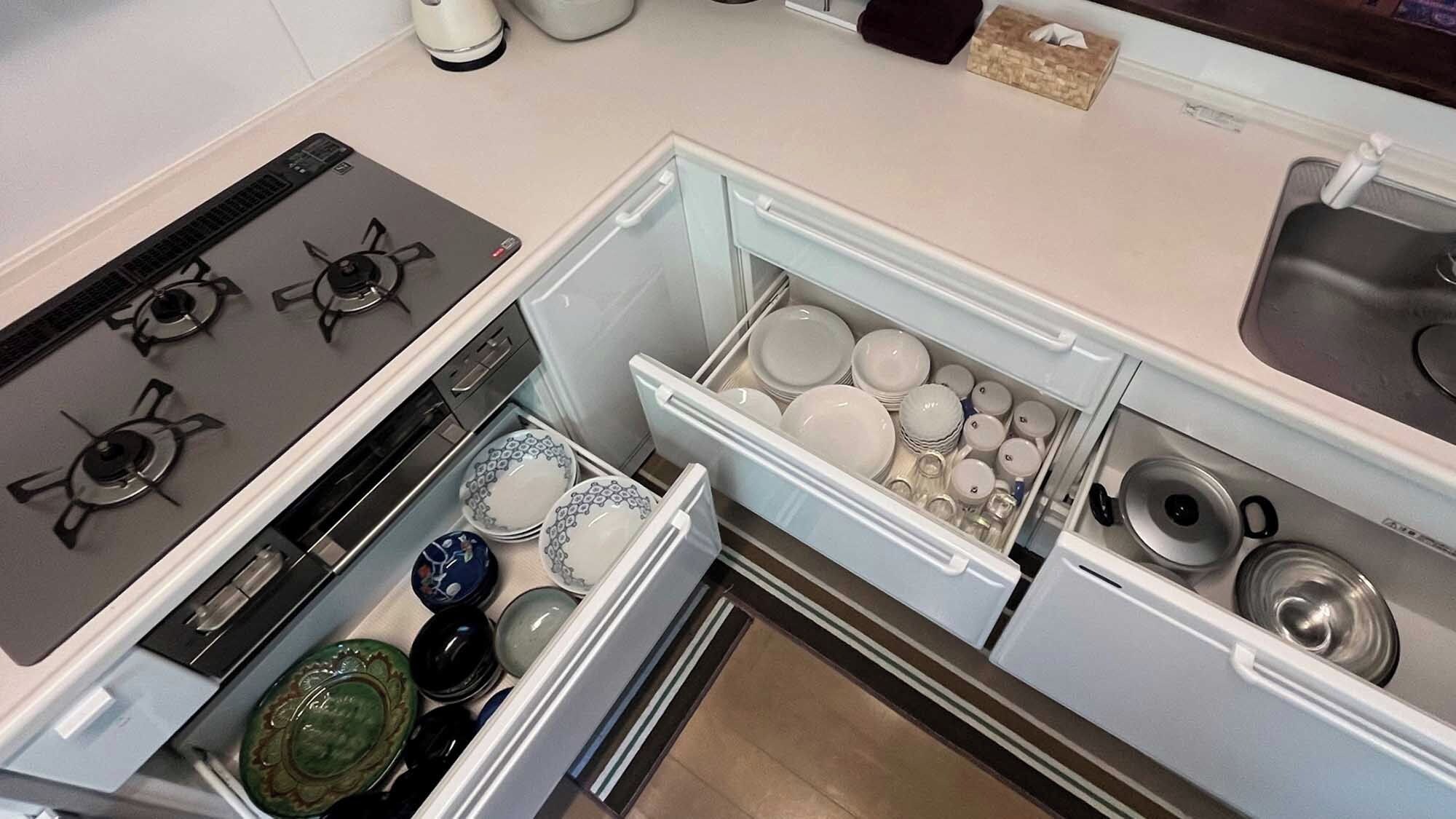 A kitchen with a stove, a refrigerator with a drawer containing dishes, and a sink.