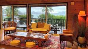 Una habitación acogedora con suelo de madera, un sofá con cojines amarillos, una mesita de café y vistas al océano a través de amplios ventanales.