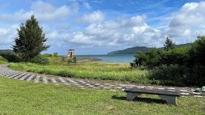 A pathway leading to a beach with a lifeguard tower, grassy areas, and a bench. - Villa Adanrose Amami (Amami)
