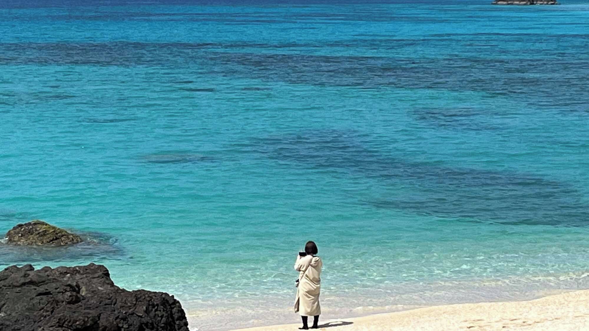 A person standing on a beach with clear turquoise water.