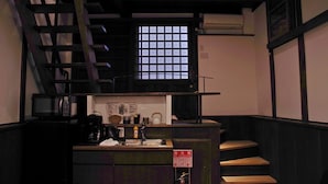 Een keukenhoek met een magnetron, waterkoker en spoelbak. Op de muur hangt een bord met daarop het brandblusser symbool en er is een raam met een rasterpatroon.