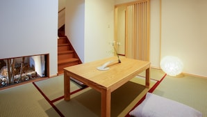 Ein traditioneller japanischer Raum mit Tatami-Böden, einem niedrigen Holztisch, einer Blumenvase, einer Hängeleuchte und einer Schiebetür.
