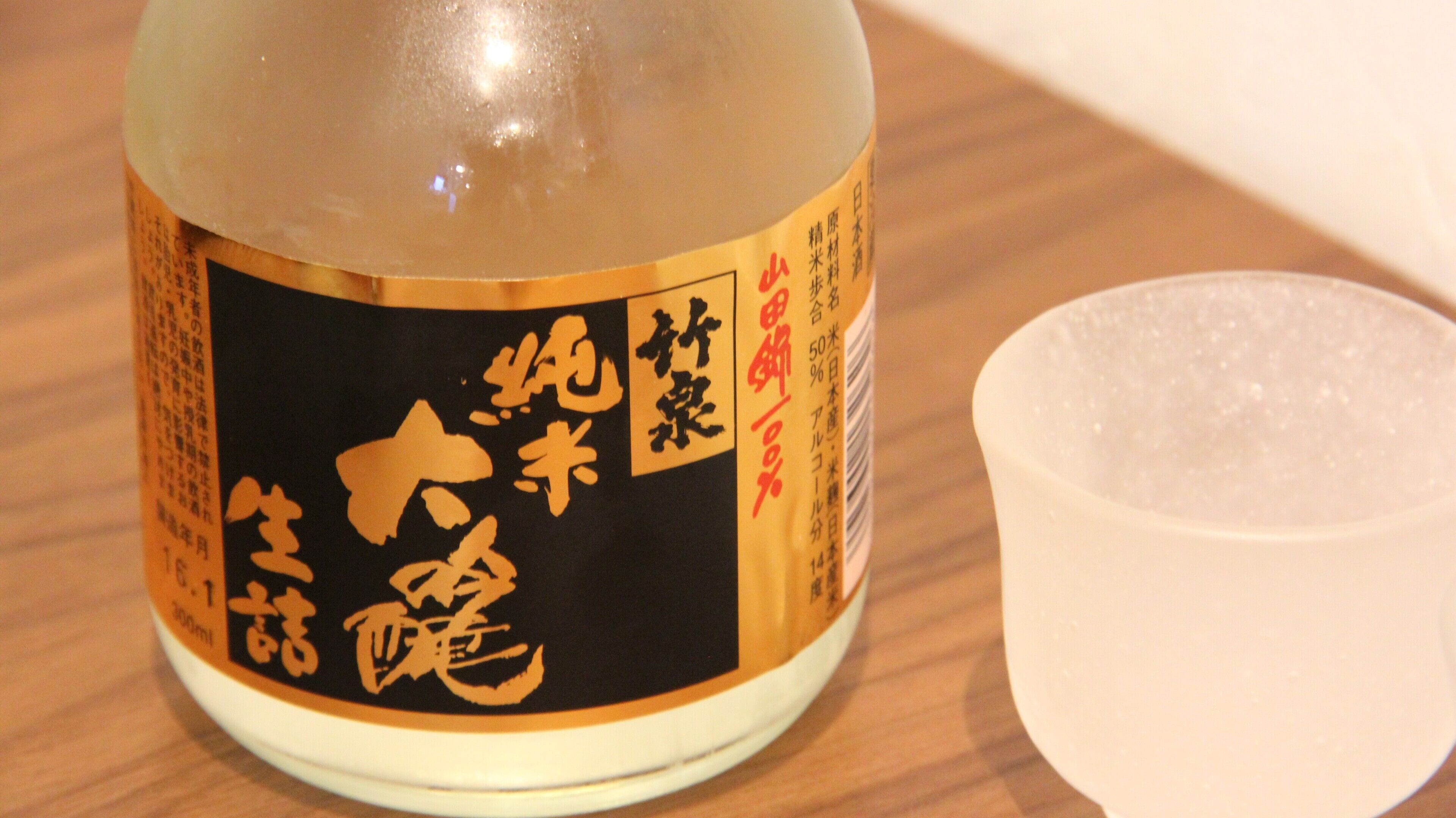 Eine Flasche mit einem Etikett mit japanischen Schriftzeichen und einer kleinen Tasse daneben.