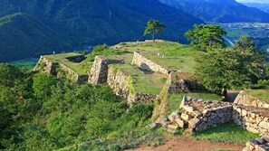 Vestiges de constructions anciennes en pierre, avec vue sur une vallée et des montagnes en arrière-plan.
