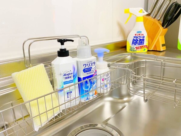 A kitchen sink area with a metal rack holding a yellow sponge, a bottle of liquid soap, and a spray bottle. - Palm Villa Ishigakijima Yugafu (Ishigaki)