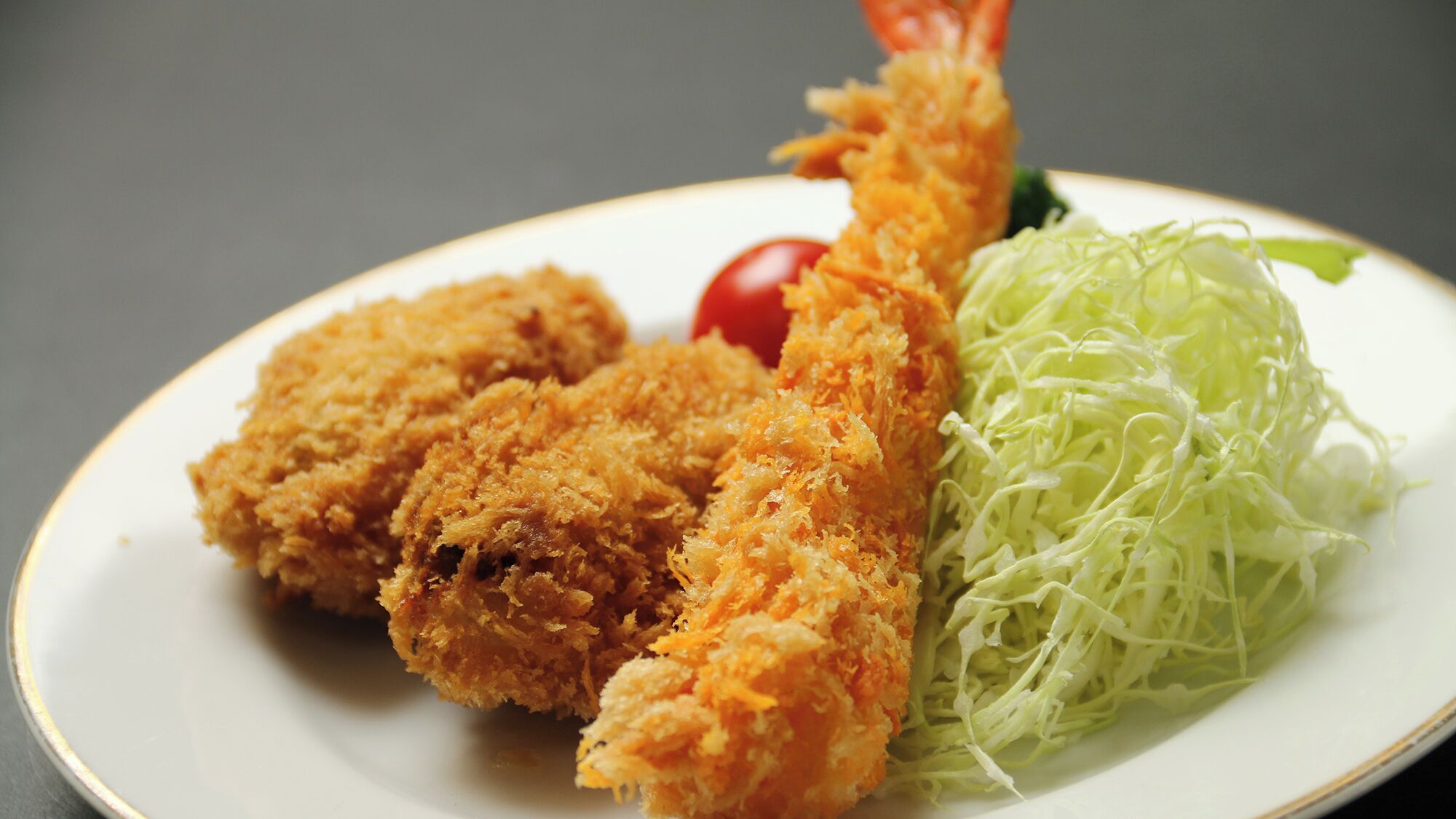 A plate with two breaded and fried items, a small cherry tomato, and shredded lettuce.