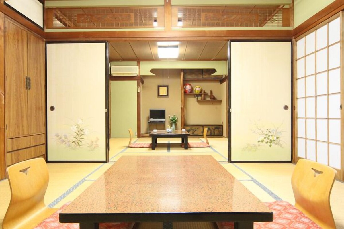 Une pièce de style japonais traditionnel, avec un sol recouvert de tatamis, une table basse et des portes coulissantes ornées de motifs floraux.