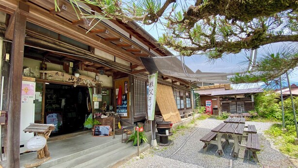 A traditional wooden building with a shop entrance, outdoor seating, and a small garden area. - Minshuku Sampo (Chichibu)