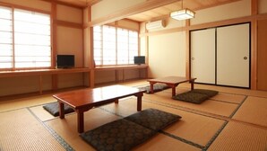 Um quarto japonês tradicional com tatames, uma mesa baixa, almofadas, portas deslizantes e uma televisão.