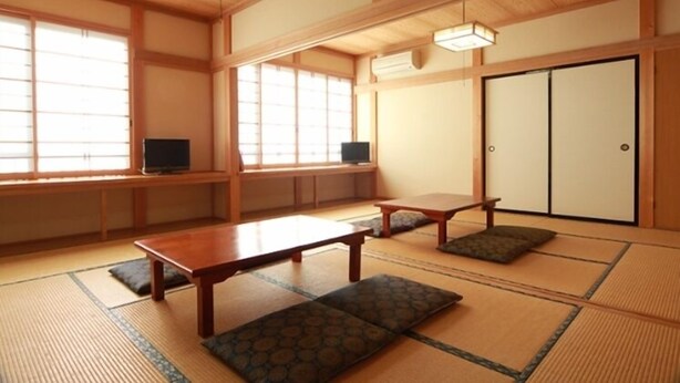 A traditional Japanese room with tatami flooring, a low table, cushions, sliding doors, and a television. - Marutomiso (Fujikawaguchiko)