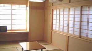 A traditional Japanese room with tatami flooring, a low table, sliding shoji doors, and a ceiling fan. - Marutomiso (Fujikawaguchiko)