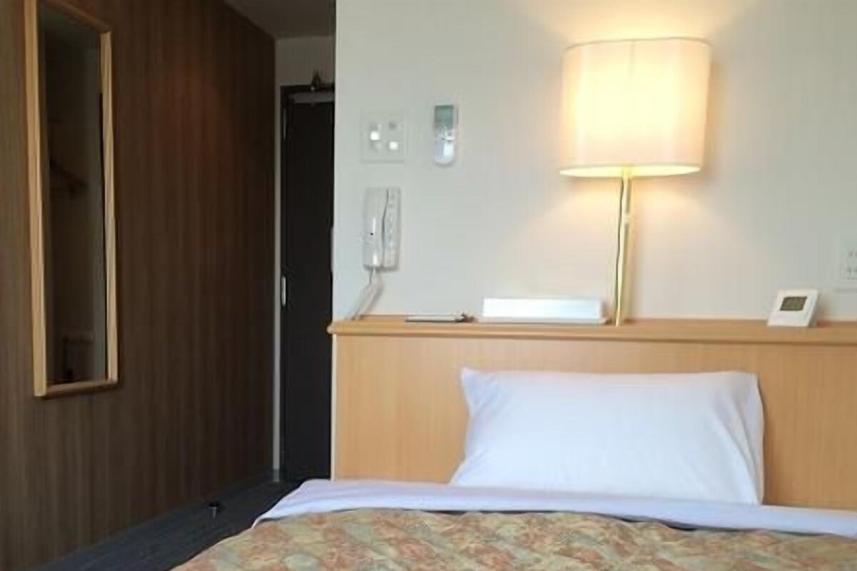 Habitación de hotel con cama, lámpara de noche, espejo y teléfono en la pared.