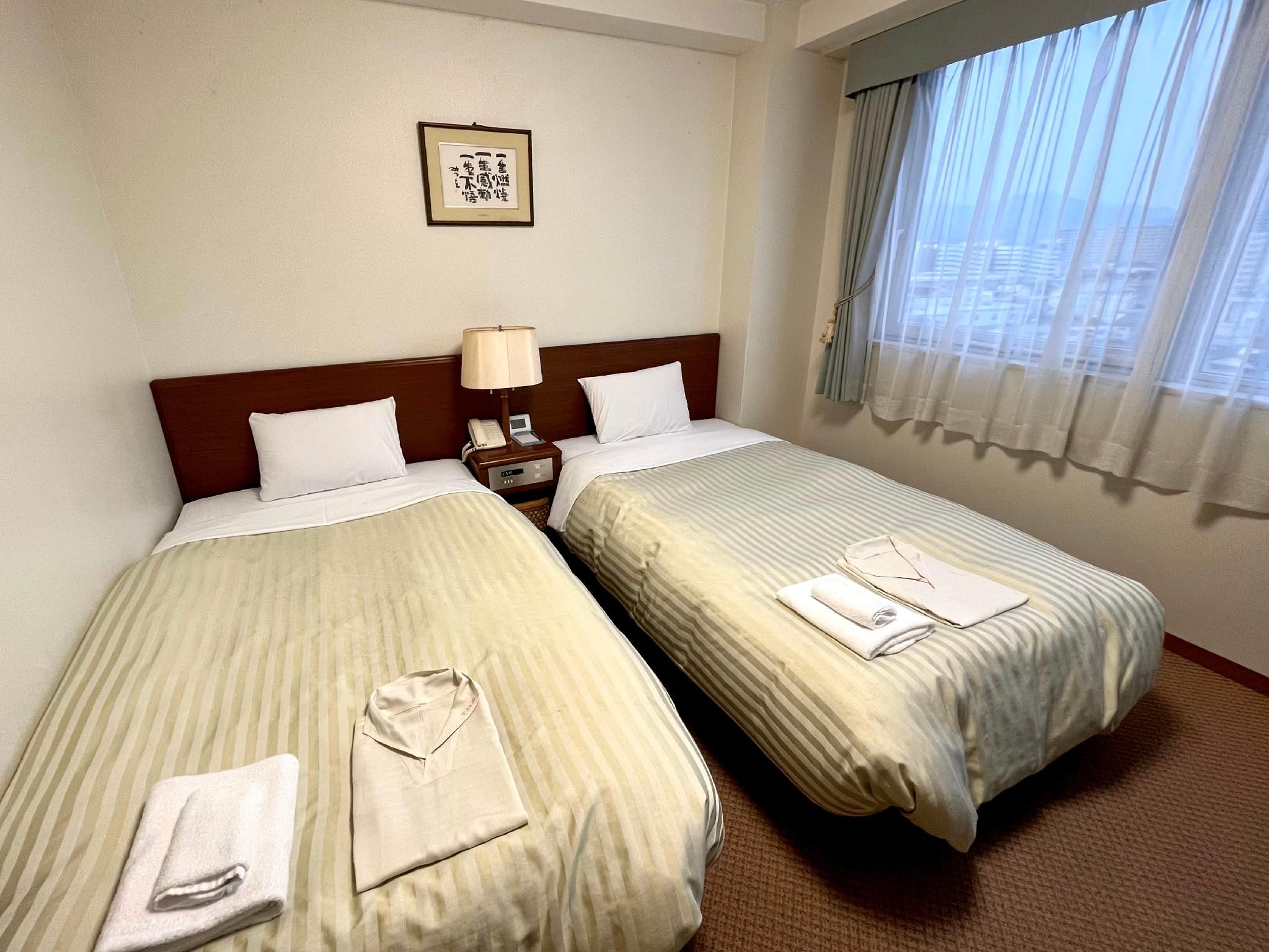 Ein Hotelzimmer mit zwei Betten, einem Nachttisch, einer Lampe und einem gerahmten Bild an der Wand.
