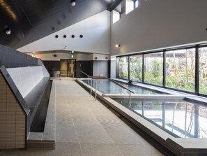 A modern indoor swimming pool with a glass barrier, a staircase on the left, and a view of greenery outside. - Shizuoka Hotel Tokinosumika (Shizuoka)