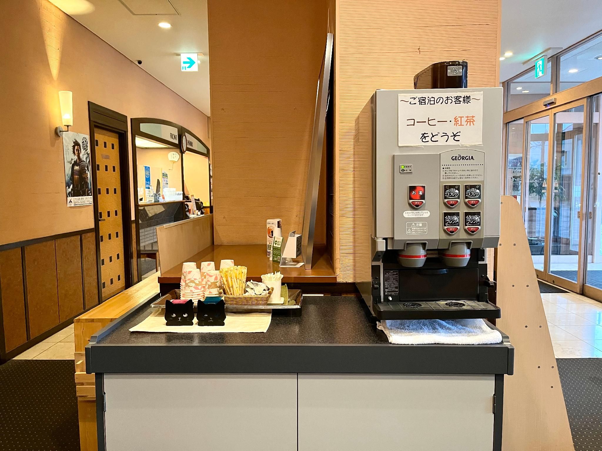 Zona de recepción de hotel con una cafetera, un mostrador con aperitivos y un espejo.
