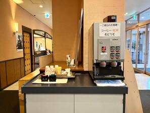 Uma área de recepção de hotel com uma máquina de café, um balcão com lanches e um espelho.