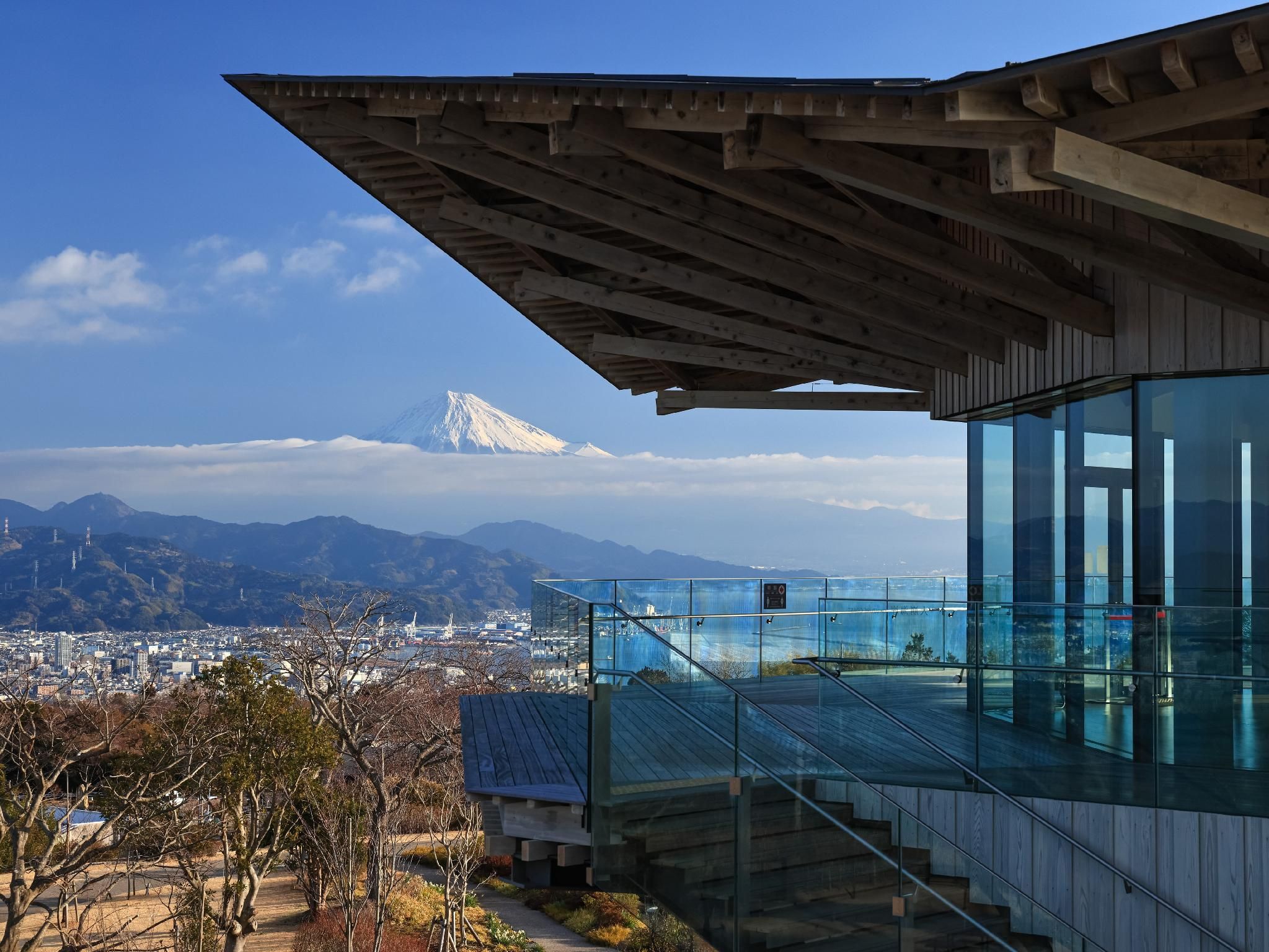 A modern building with a glass facade overlooking a cityscape and a mountain.