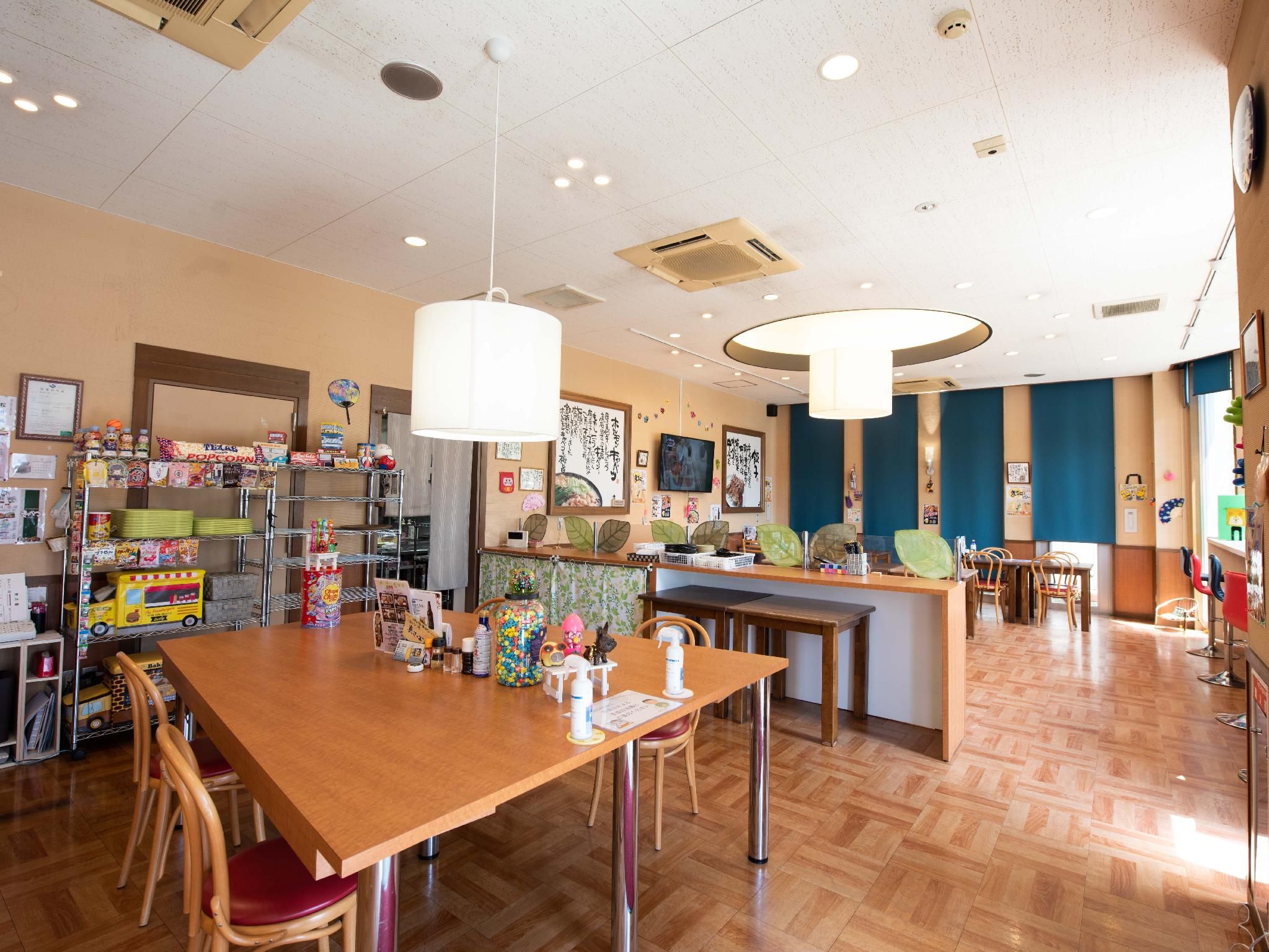 Ein Restaurant mit Holztischen, Stühlen und einer Auswahl an Lebensmitteln, die in Regalen präsentiert werden.