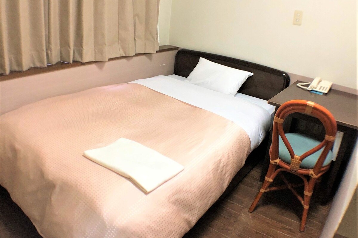 A hotel room with a bed, a chair, a desk, and a telephone.