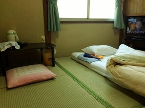 Habitación de hotel con cama, un pequeño escritorio, un cesto de basura y televisor.