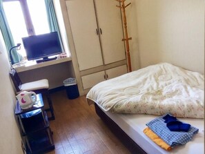 Un dormitorio con una cama, un escritorio con ordenador, una silla, una ventana con cortinas y un armario.
