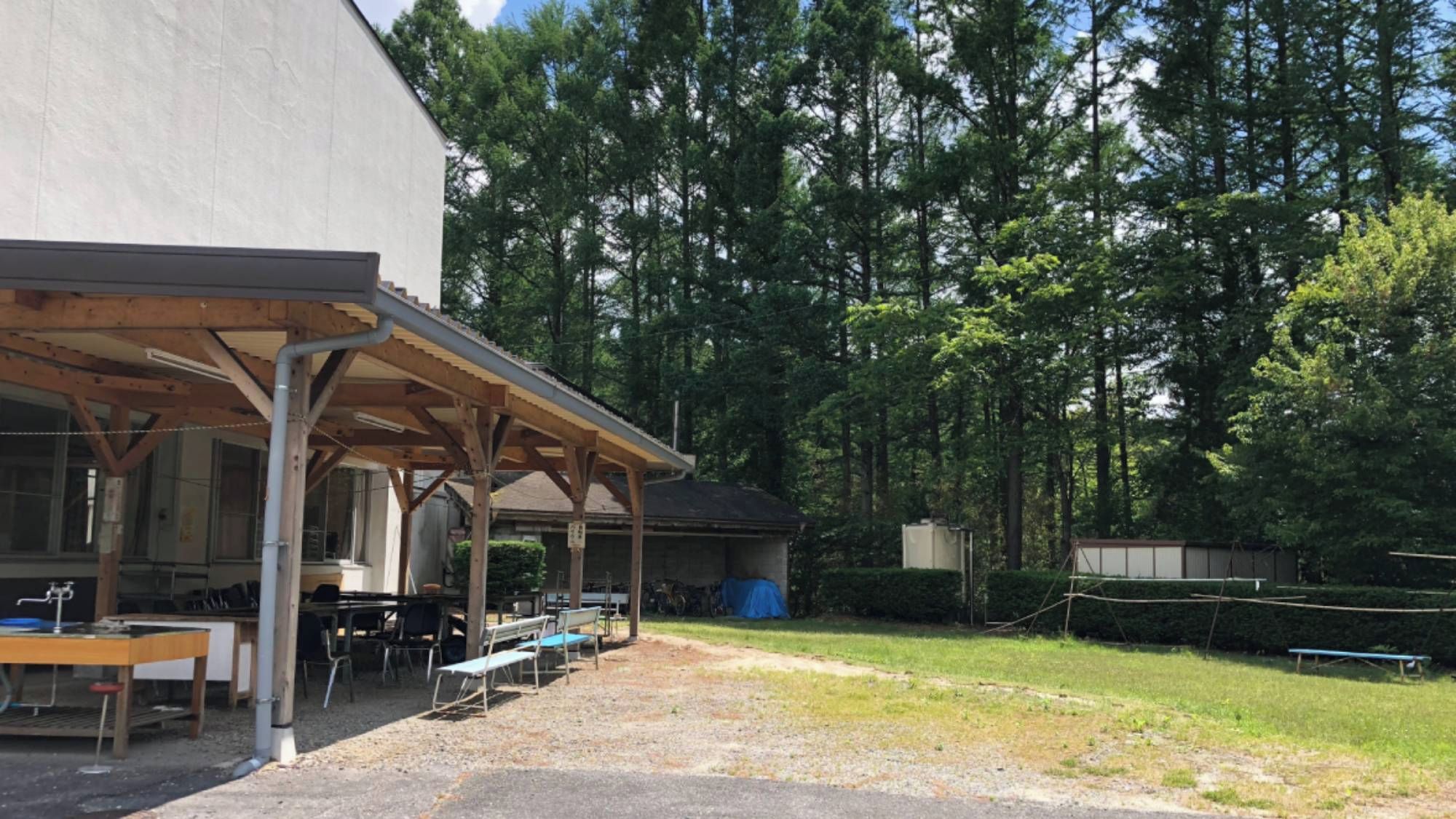 An outdoor covered area with tables and chairs, surrounded by trees.