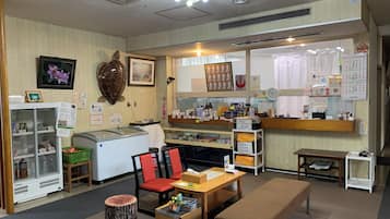 Ein Zimmer mit einer Rezeption, einem Kühlschrank, einer Holzbank und einem kleinen Tisch mit Stühlen.