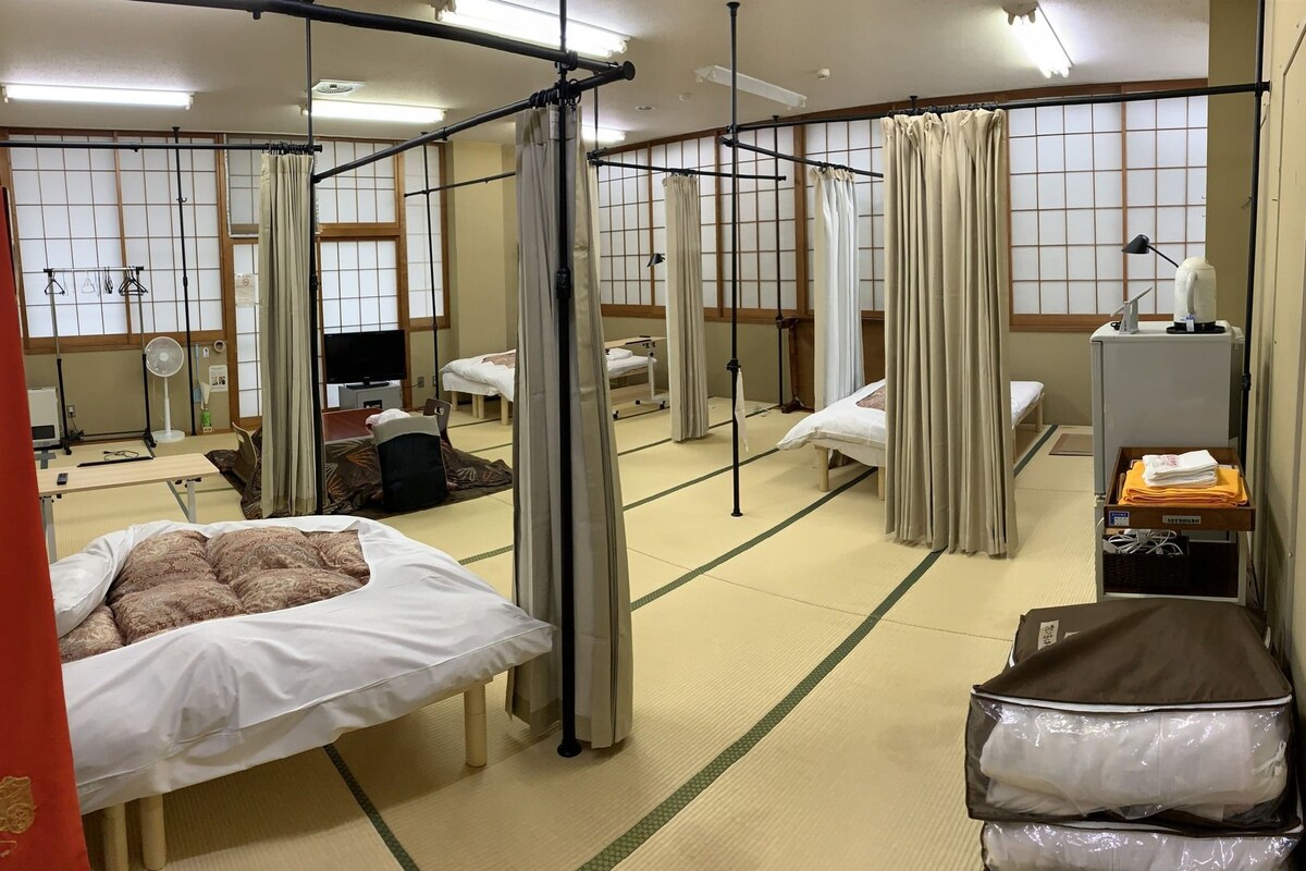 A traditional Japanese-style room with tatami flooring, multiple beds, a television, and a futon.