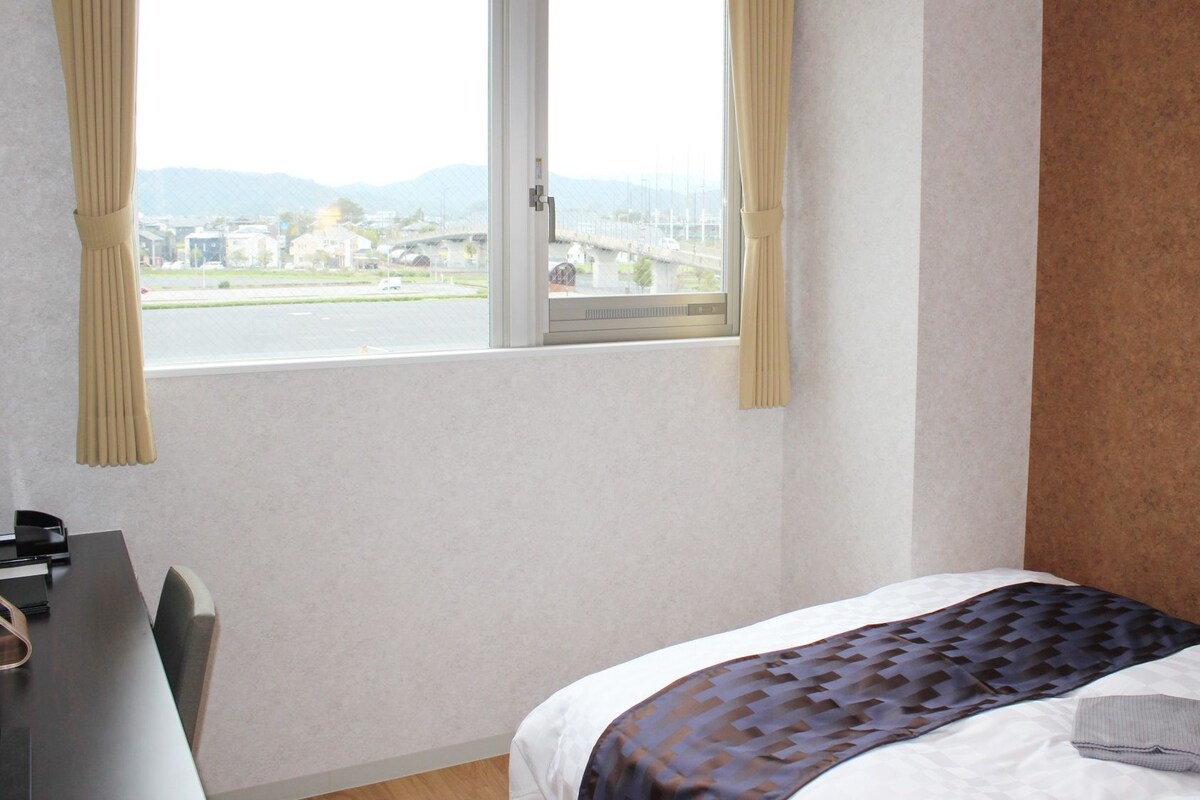 A hotel room with a bed, a desk, and a window with curtains.