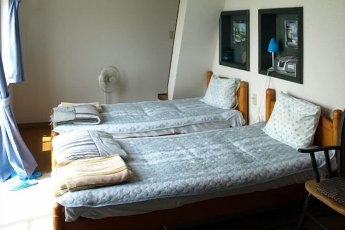 A room with two beds, a bunk bed above, a fan, and a window with pictures.