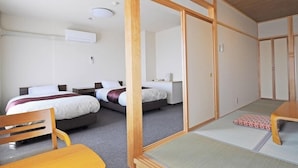 Habitación de hotel con dos camas, un escritorio, una silla y una puerta corredera tradicional japonesa.