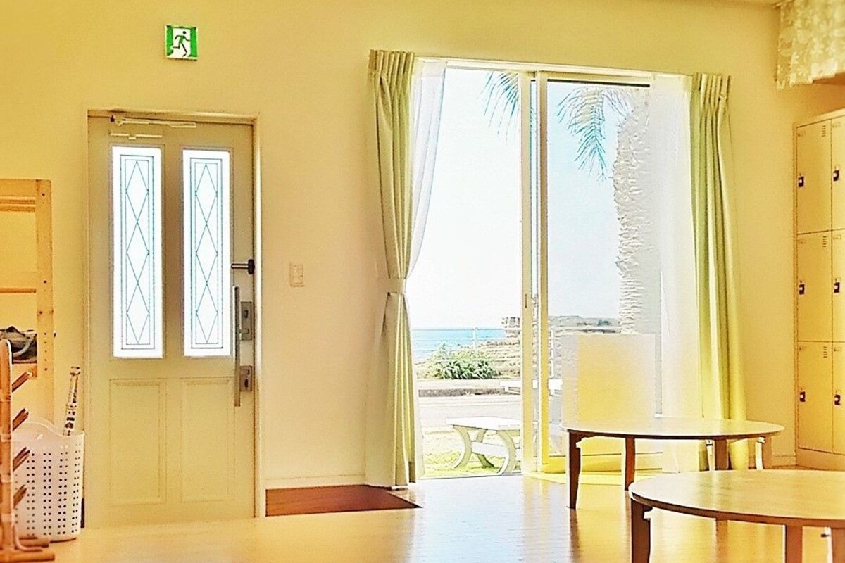 A room with a wooden floor, a door with glass panels, a table, and a view of the outdoors through a glass door with curtains.