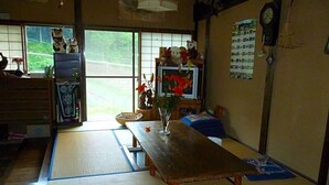 A traditional Japanese room with tatami flooring, a wooden table, a vase with flowers, and a view of greenery outside. - Minshuku Yurika (Urugi)