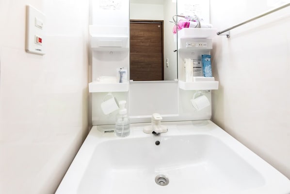 A bathroom with a white sink, a mirror, and a door. There are toiletries on the wall and a towel rack.
