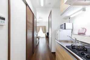 Un couloir étroit mène à une chambre dotée d’un lit, d’une kitchenette équipée d’un four à micro-ondes, d’une bouilloire et d’une cuisinière à gaz.