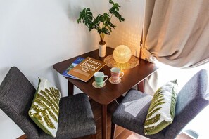 Une petite table sur laquelle se trouvent un livre, une plante et une lampe décorative. Deux chaises, dotées de coussins à motifs, sont placées à proximité.